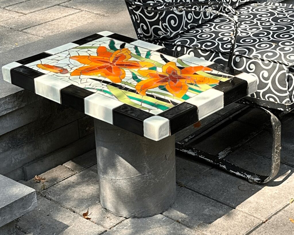 floral motif trencadis mosaic tile tabletop mounted to concrete base next to outdoor furniture on a patio