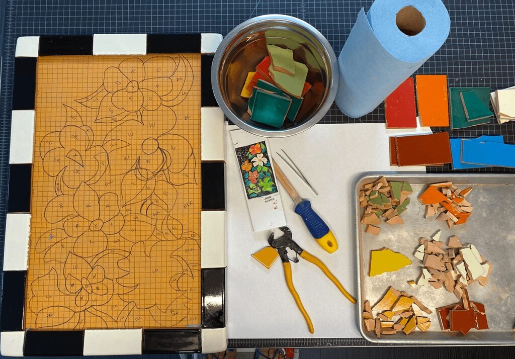 kerdi-board tabletop with transferred design motif in place ready to tile, alongside tools and broken mosaic tile